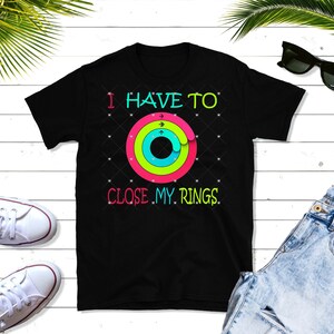 Op de afbeelding: Zwart T-shirt met een kleurrijke afbeelding van een ring met de tekst "Ik moet mijn ringen sluiten".