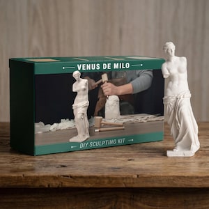 May include: A white Venus de Milo statue stands next to a box labeled "Venus de Milo DIY Sculpting Kit." The box features a green border and an image of someone sculpting. The kit includes tools and a small statue.