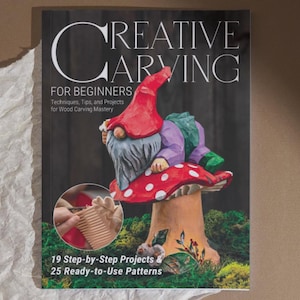 Pode incluir: A capa do livro "Creative Carving for Beginners" apresenta um gnomo esculpido colorido em um cogumelo vermelho com bolinhas brancas. O gnomo usa um chapéu vermelho e roupas roxas. O título e subtítulo do livro também são visíveis.