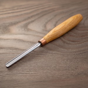May include: A wood carving gouge featuring a polished steel blade with a curved profile and a smooth, light-colored wooden handle. The tool includes a copper-colored metal ferrule connecting the blade to the handle, showing a clear grain pattern.