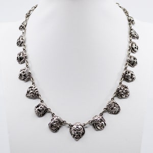 May include: A silver necklace with a chain and multiple pendant charms. Each charm is a detailed, textured, silver face.