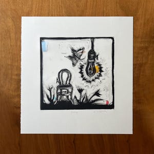 May include: Black and white artwork of a chair, butterfly, and lightbulb. The lightbulb is lit with yellow and white bursts. The word "Energy" is written at the bottom of the artwork. The artwork is framed in a white mat.