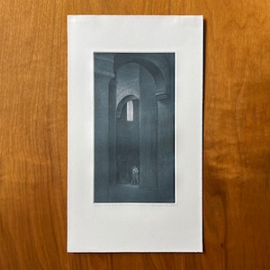 May include: A black and white print of a hallway with a single figure standing in the distance. The hallway is lined with columns and arches, and a small window lets in a sliver of light.