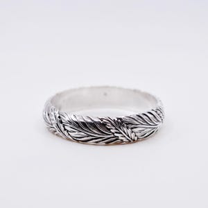 May include: A silver ring featuring a continuous embossed feather pattern around the entire band. The metal has a polished finish with darkened recessed areas that highlight the intricate details of the carved leaf-like texture.