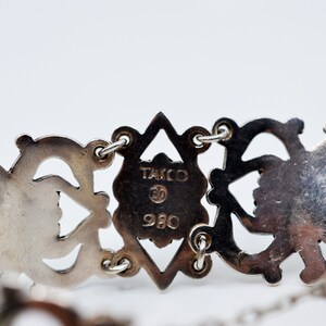 May include: Close-up of a silver bracelet with an intricate design. The back of the bracelet has the inscription "Taxco 980" in a diamond-shaped design.