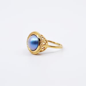May include: A gold ring with a blue pearl set in a decorative, openwork setting.