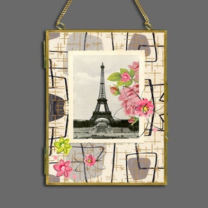 May include: A gold-framed picture with a vintage design featuring a black and white image of the Eiffel Tower in Paris, France. The picture is surrounded by pink and green flowers and has a gold chain for hanging.