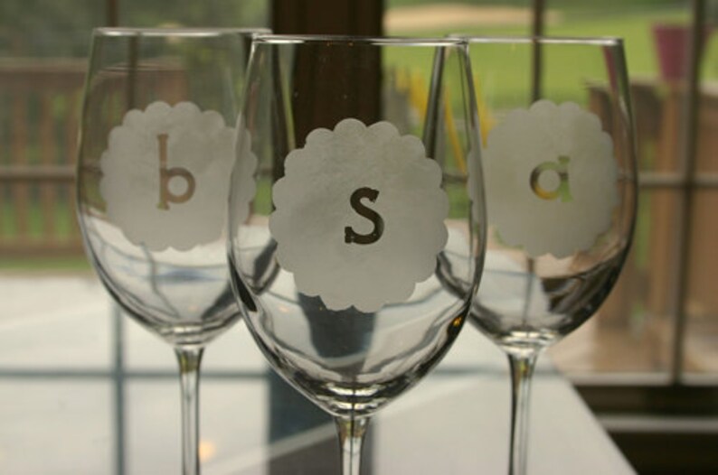 Puede incluir: Tres copas de vino de vidrio transparente con las letras 'b', 's' y 'a' grabadas en la parte delantera. Las copas est&aacute;n sobre una superficie blanca.