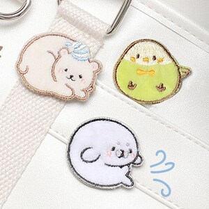 May include: Three embroidered iron-on patches featuring a sleeping bear, a bird, and a seal. The patches are on a white background.