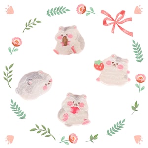 May include: Four embroidered iron-on patches featuring cute cartoon hamsters with pink cheeks. The hamsters are holding a strawberry, a piece of food, and a heart. The patches are surrounded by pink flowers and green leaves.