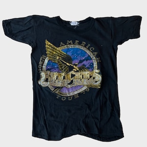May include: Black t-shirt with a gold and purple graphic of a flying eagle and the text "North American Tour '79" with the band name "Bad Company" in a stylized font.
