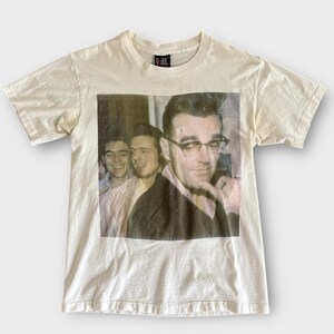 May include: Cream-colored t-shirt featuring a vintage-style photograph of three men, one wearing glasses and a blazer. The shirt has a crew neck and short sleeves. The brand name "g-ant" is printed on the collar.
