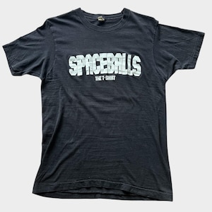 Op de afbeelding: Donkergrijs t-shirt met de witte tekst "SPACEBALLS" in blokletters. Daaronder staat de tekst "THE T-SHIRT". De stof lijkt zacht en licht gekreukt.