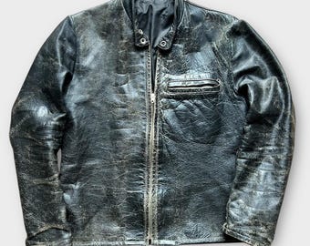 Puede incluir: Chaqueta de cuero negro desgastado con cremallera, un pequeño bolsillo en el pecho y cuello alzado. La chaqueta tiene un aspecto vintage con textura visible y variaciones de color sutiles. Prenda de abrigo clásica.