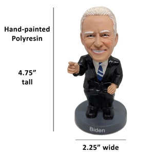 May include: Hand-painted polyresin figurine of a person with a smiling face, wearing a black suit and blue tie. The figurine is 4.75 inches tall and 2.25 inches wide. The base of the figurine is gray and has the word "Biden" written on it.