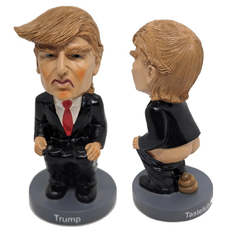 May include: A figurine of a person in a black suit and red tie, with a brown hairstyle. The figurine is in a seated position with the text "Trump" on the base. The figurine is also shown from the back, with the text "Tastefully Offensive" on the base.