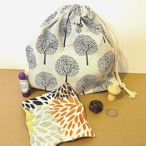 May include: A white drawstring bag with a black tree pattern, a small pouch with a floral pattern, a wooden bead, a dark brown stone, a silver ring, and a purple tube with the text "Lavender Lotion" on it.