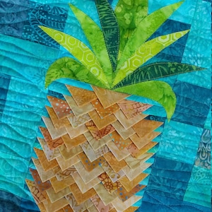 Könnte beinhalten: Ein gestepptes Ananas-Design mit grünem Oberteil und gelbem Körper. Die Ananas befindet sich auf einem blauen und weißen Patchwork-Hintergrund.