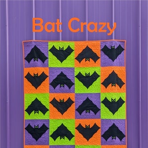 Può includere: Un muro viola con una trapunta appesa. La trapunta è fatta di quadrati arancioni, verdi e viola con pipistrelli neri su ogni quadrato. La trapunta è intitolata "Bat Crazy" e ha un cerchio nero con testo bianco che dice "Slice of Pi Quilts" in basso.