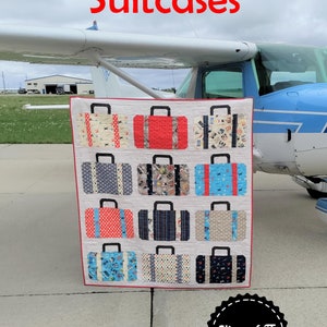May include: A quilt with a patchwork design of suitcases in various colors and patterns. The quilt is displayed in front of a small airplane. The quilt is titled "Suitcases" and the artist's name is "Slice of Pi Quilts".