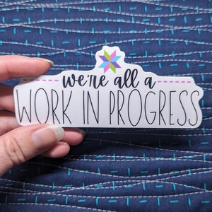 Quilt sticker with phrase "we're all a work in progress"