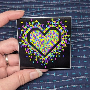 May include: A sticker with a black background and a colorful heart made of triangles. The heart is outlined in yellow and filled with pink, blue, green, and yellow triangles.