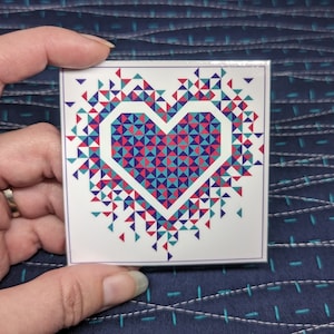 May include: A white square tile with a red, blue, and teal geometric heart design. The heart is made up of small triangles that form a larger heart shape.