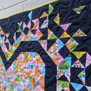 A colorful Mini Exploding Heart quilt made with a navy background fabric hanging on a wall
