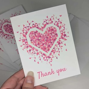May include: A stack of thank you cards with a pink geometric heart design and the text "Thank you".