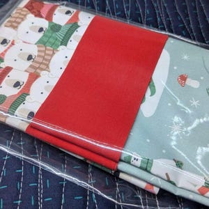 May include: A set of three fabric squares featuring a winter theme. The first square has a white background with a repeating pattern of polar bears wearing hats and scarves. The second square is solid red. The third square has a light blue background with a repeating pattern of polar bears wearing scarves and hats, snowflakes, and mushrooms.