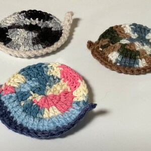 May include: Three crocheted snail ornaments in different color patterns. The snails are made with white, black, brown, blue, pink, and cream yarn.