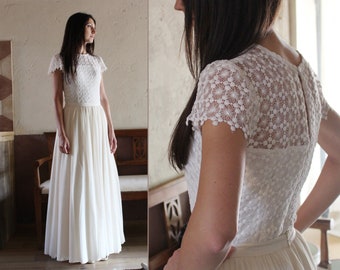 May include: A white lace wedding dress with a fitted bodice and a flowing skirt. The dress has a round neckline and short sleeves.