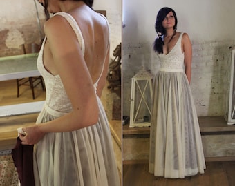 May include: A white lace and tulle wedding dress with a fitted bodice and a flowing skirt. The dress has a low back and a simple design.