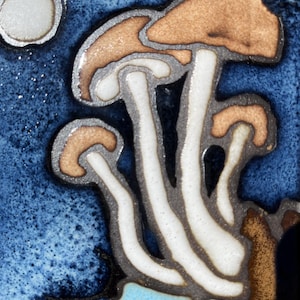 May include: A close-up of a ceramic tile featuring a stylized mushroom design. The mushrooms have brown caps, white stems, and are outlined in gray. The background is a textured blue with a white moon.