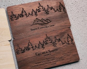 Op de afbeelding: Twee lichtgekleurde houten visitekaartjes voor Mike Harrison, Precision Woodworker, met een zaagbladlogo en contactgegevens, naast twee donkergekleurde houten visitekaartjes voor George Smith Construction met een bosafbeelding.
