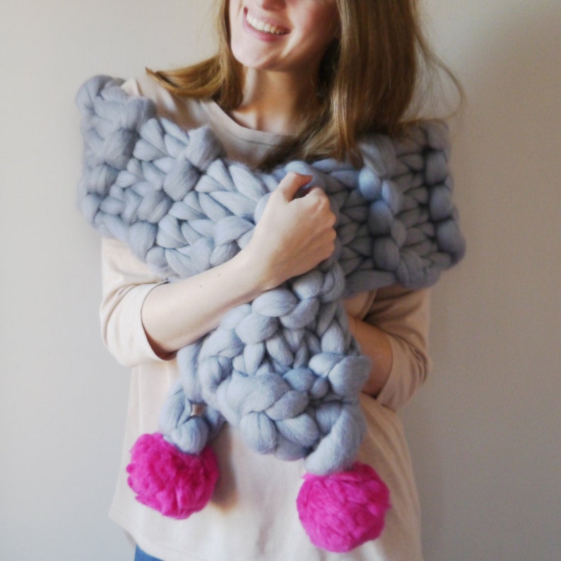 May include: A gray chunky knit scarf with large pom poms in a bright pink color.