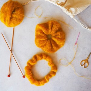 K&ouml;nnte beinhalten: Nahaufnahme eines gelben Garnprojekts mit zwei Stricknadeln und einer Schere. Das Garn ist in Kreisform und als Knoten angeordnet.