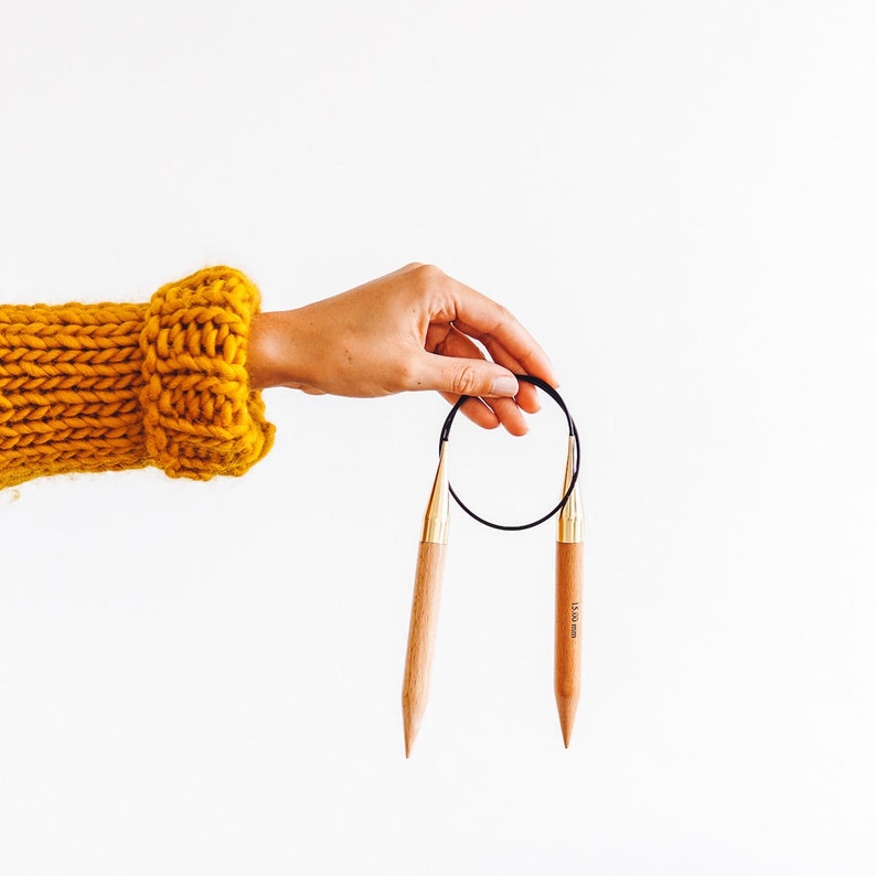 Puede incluir: Un par de agujas de tejer de madera con puntas doradas y un cord&oacute;n negro. Las agujas miden 15,00 mm.