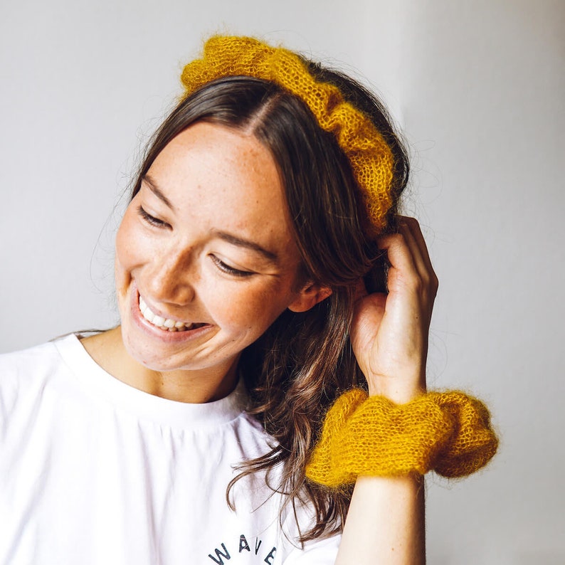 K&ouml;nnte beinhalten: Eine Frau tr&auml;gt ein gelbes Strickband und eine passende gelbe Strickmanschette. Sie l&auml;chelt und schaut nach unten. Sie tr&auml;gt ein wei&szlig;es T-Shirt mit dem Aufdruck "WAVE".