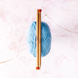 May include: A ball of light blue yarn with two wooden knitting needles, each marked "10.00 mm", sticking through the center.