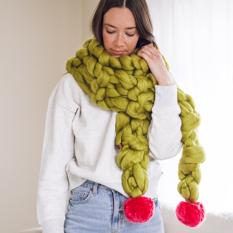 May include: A chunky knit scarf in a bright green color with two large pink pom-poms at the ends.