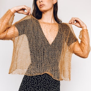 May include: A sheer, gold-colored knitted sweater with a loose fit and long sleeves. The sweater is made of a delicate, open-weave fabric.