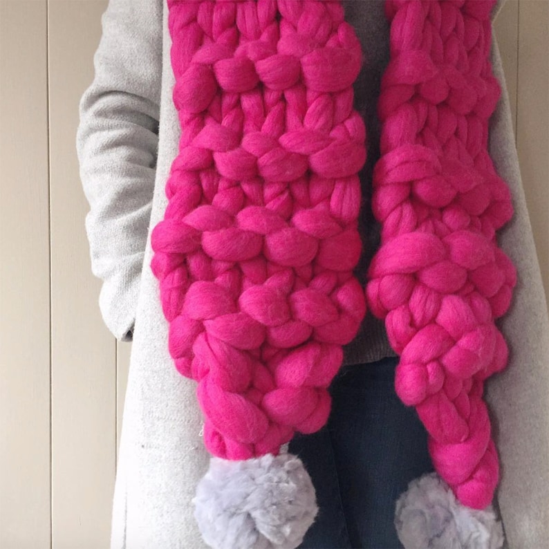 May include: A bright pink chunky knit scarf with two fluffy gray pom-poms on the ends.