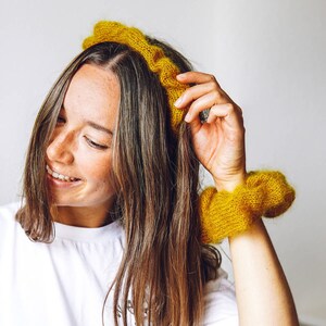 K&ouml;nnte beinhalten: Eine Frau mit langen braunen Haaren tr&auml;gt ein gelbes Strickband und ein passendes gelbes Strickhaarband am Handgelenk.