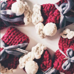 May include: Five red knitted gift bags with white pom-poms and gray ribbon bows. The bags are tied with a gray ribbon and have a small white tag that says "Love Note Design".