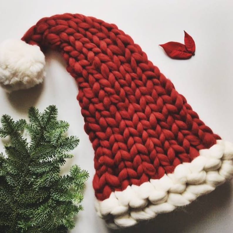 May include: A large, red knitted Santa hat with a white pom-pom on top and a white trim around the bottom.