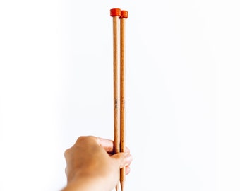 May include: Two wooden knitting needles with orange caps are held against a white background. The needles are light brown with a smooth finish. The needles are labeled with the size 4.00 mm.