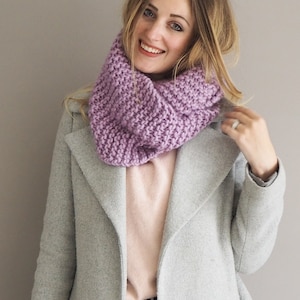 May include: A woman wearing a light gray coat with a purple infinity scarf. The scarf is knitted and has a textured pattern.
