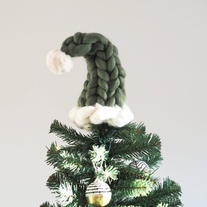 May include: A green knitted Christmas tree topper shaped like a Santa hat with a white pom-pom on top.