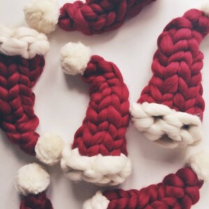 May include: A group of red and white knitted Santa hats with a braided design. The hats are made of a soft, fluffy yarn.